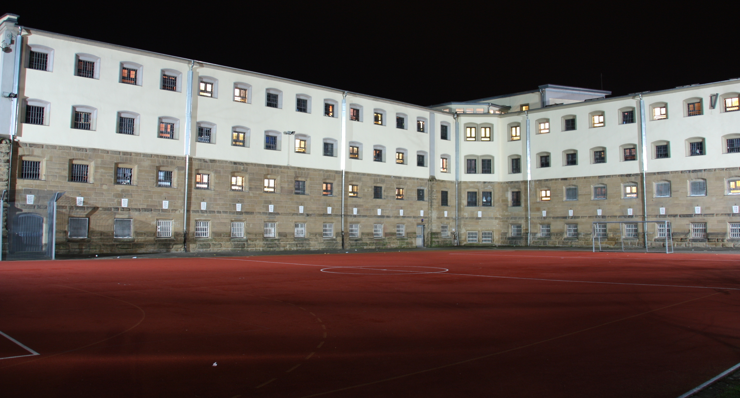 Blick über den Sporthof in Richtung Haftgebäude bei Nacht